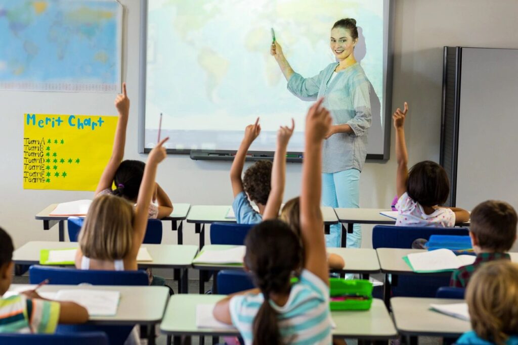 A person standing in front of the students sitting and raising their hands