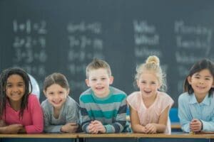 Five elementary students smiling in front of chalkboard